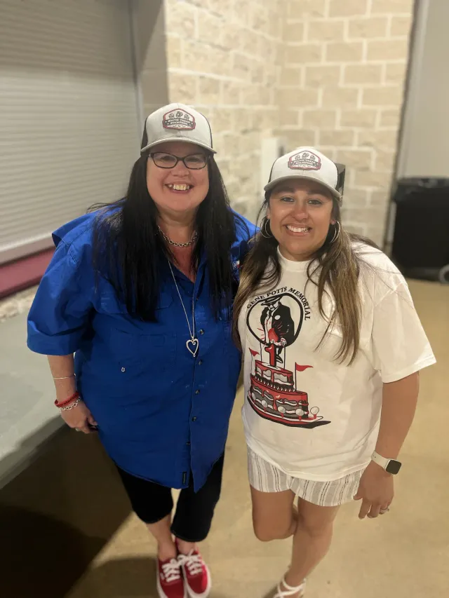 Two women in caps pose together beside a doorway.