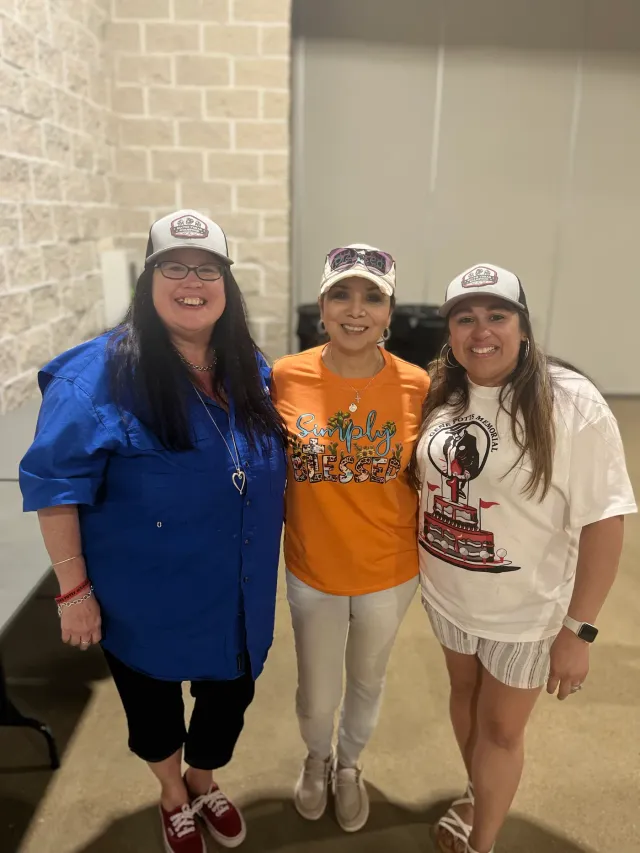 Three women in caps pose together inside the event hall.