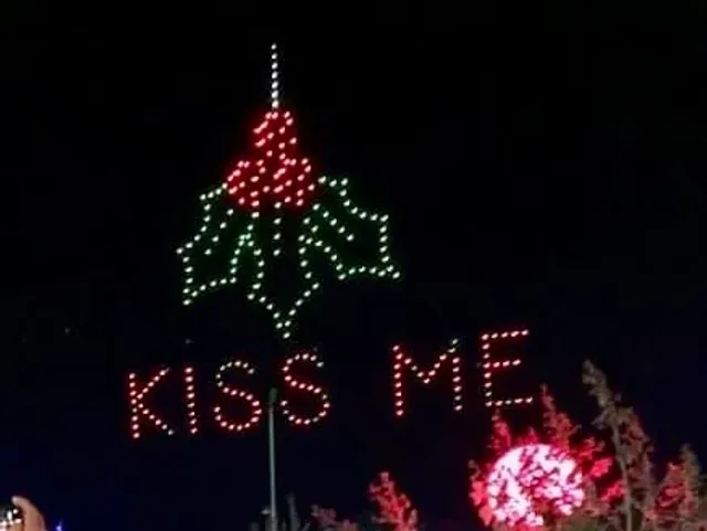 A holly-themed light display spells Kiss Me against the night sky.