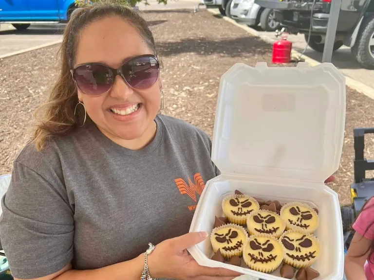 A woman displays a box of decorated cookies outdoors.