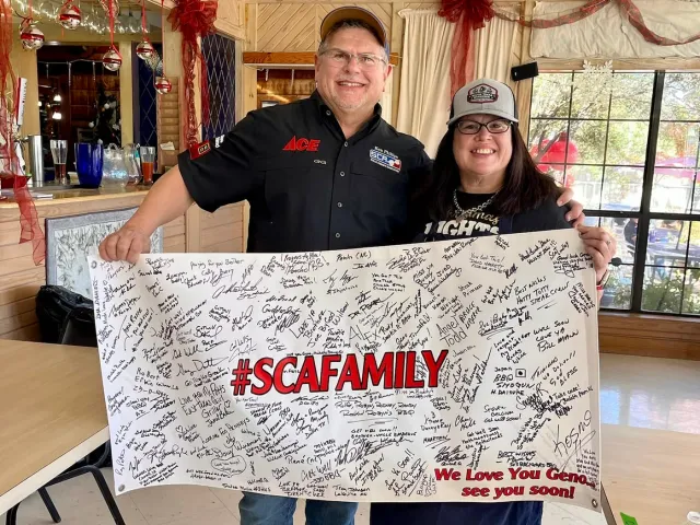 Two adults hold a signed banner bearing the hashtag SCAFamily.
