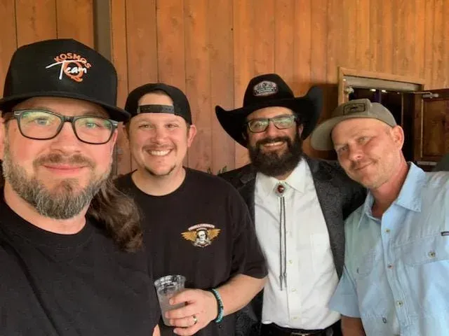Four men pose together in front of a wood-paneled wall.