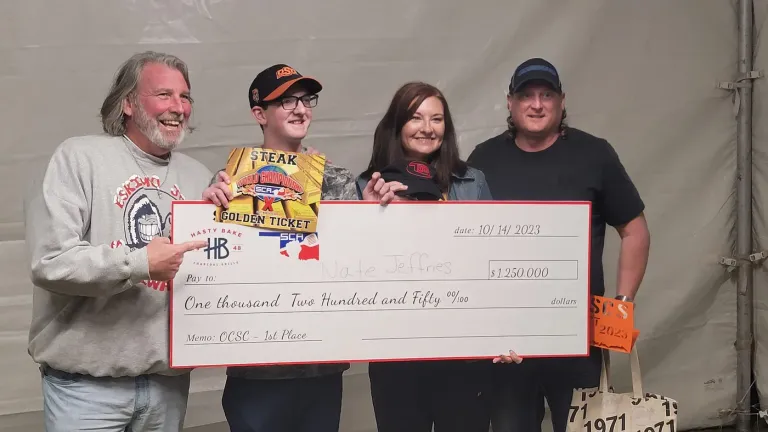 Four people pose with an oversized prize check and a trophy.