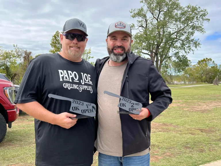 Two men pose outdoors holding rectangular award plaques.