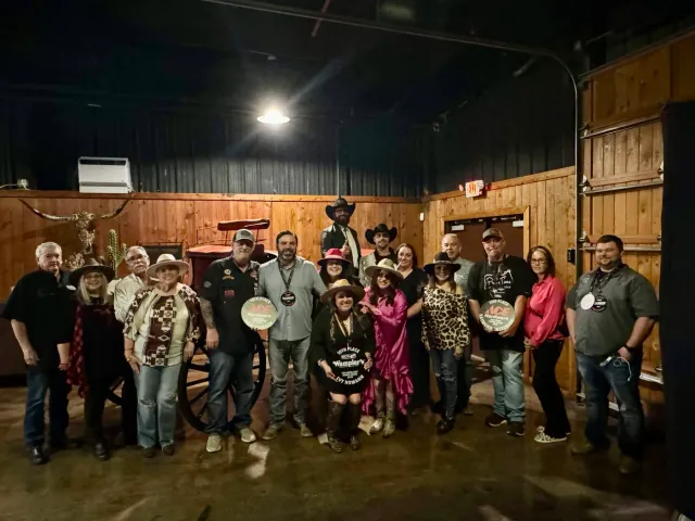 A group poses with awards against a wood-paneled wall beneath longhorn horns.