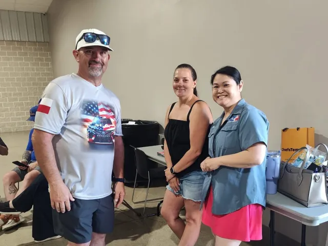 A man and two women pose beside tables inside the event hall.