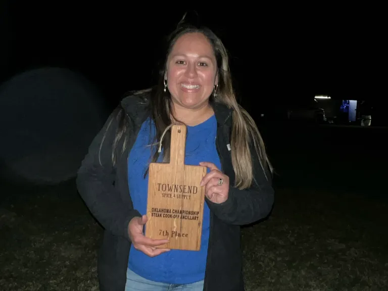 A woman holds a wooden award plaque outdoors at night.