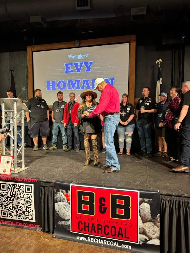 Awards participants stand on stage beside a presenter in a red shirt.