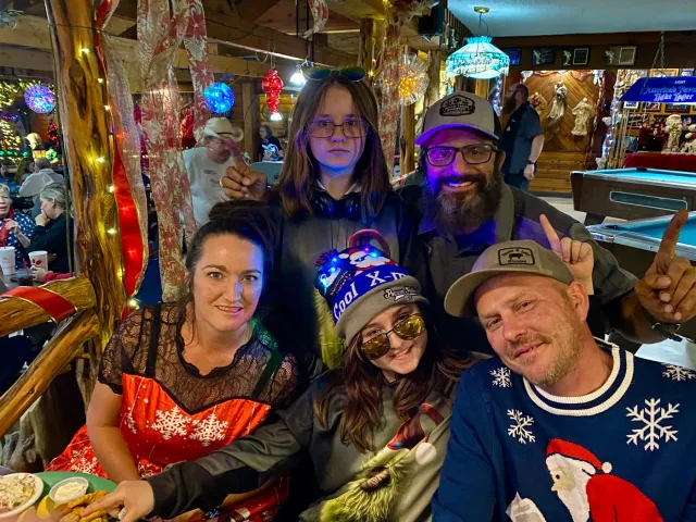 Five people pose together beneath colorful holiday decorations indoors.