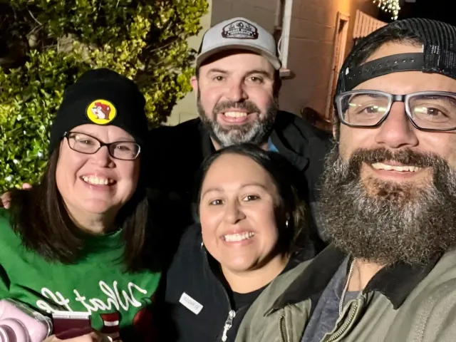 Four smiling adults pose for a close-up photo outdoors at night.