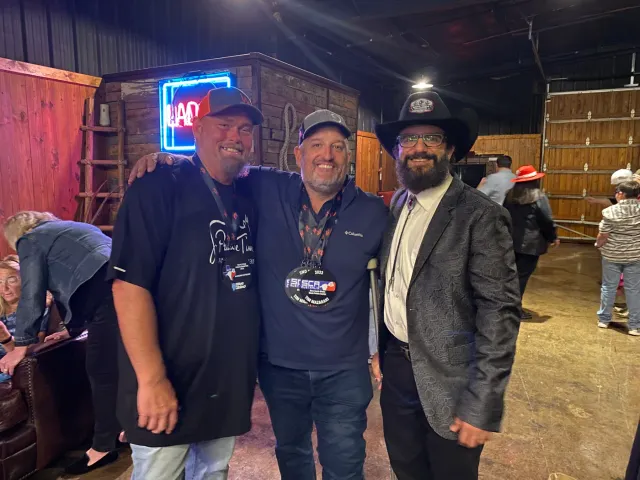 Three men pose together at an indoor gathering.