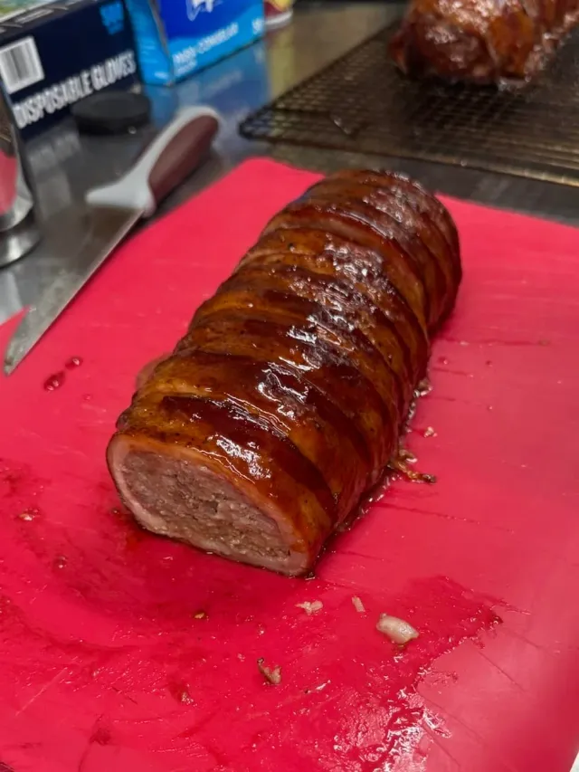 A glazed meat roll with one end sliced rests on a red cutting board.