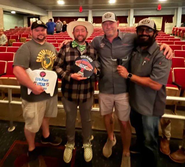 Four men pose with awards in front of rows of red auditorium seats.