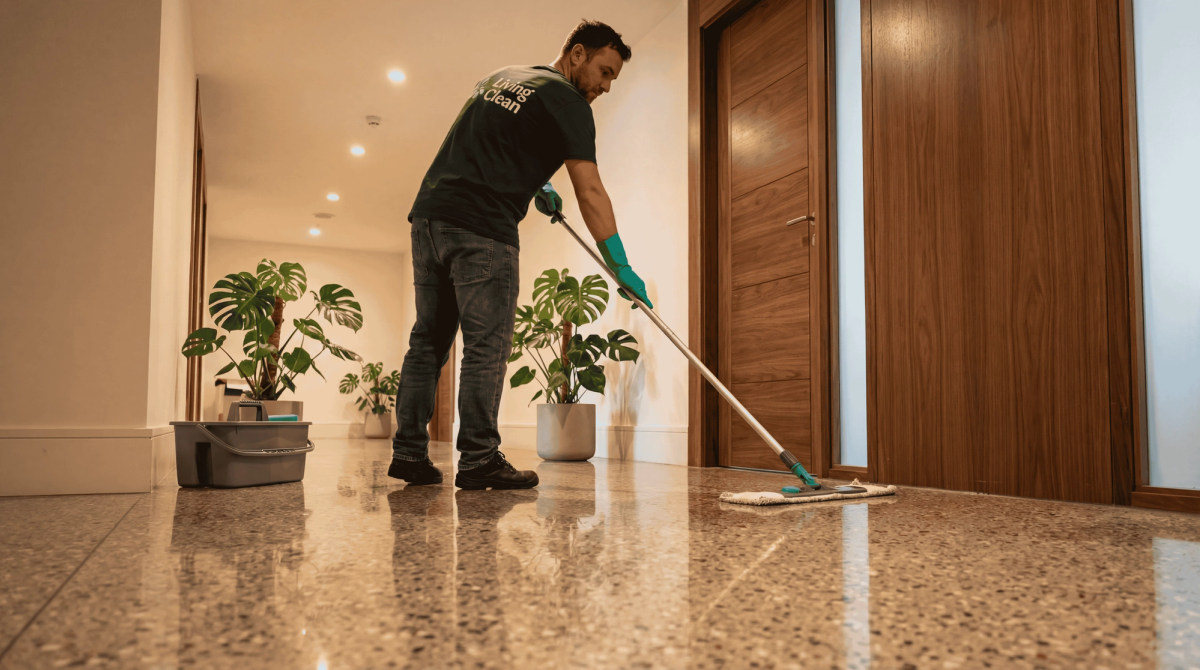 Living Clean-ansatt vasker steingulv i en gang med potteplanter og tredører.