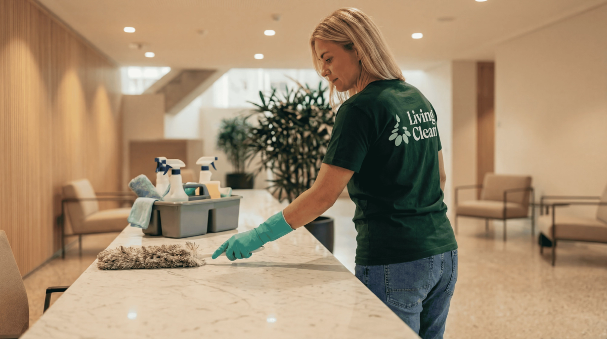 Living Clean-ansatt vasker en resepsjonsdisk med rengjøringsmidler i en kontorlobby.