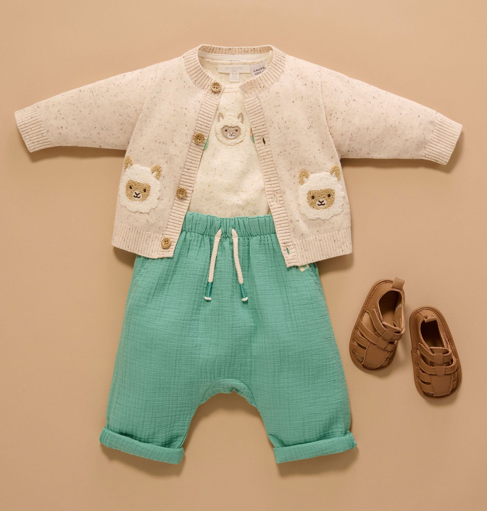 Baby outfit of beige cardigan, green pants and tan sandals