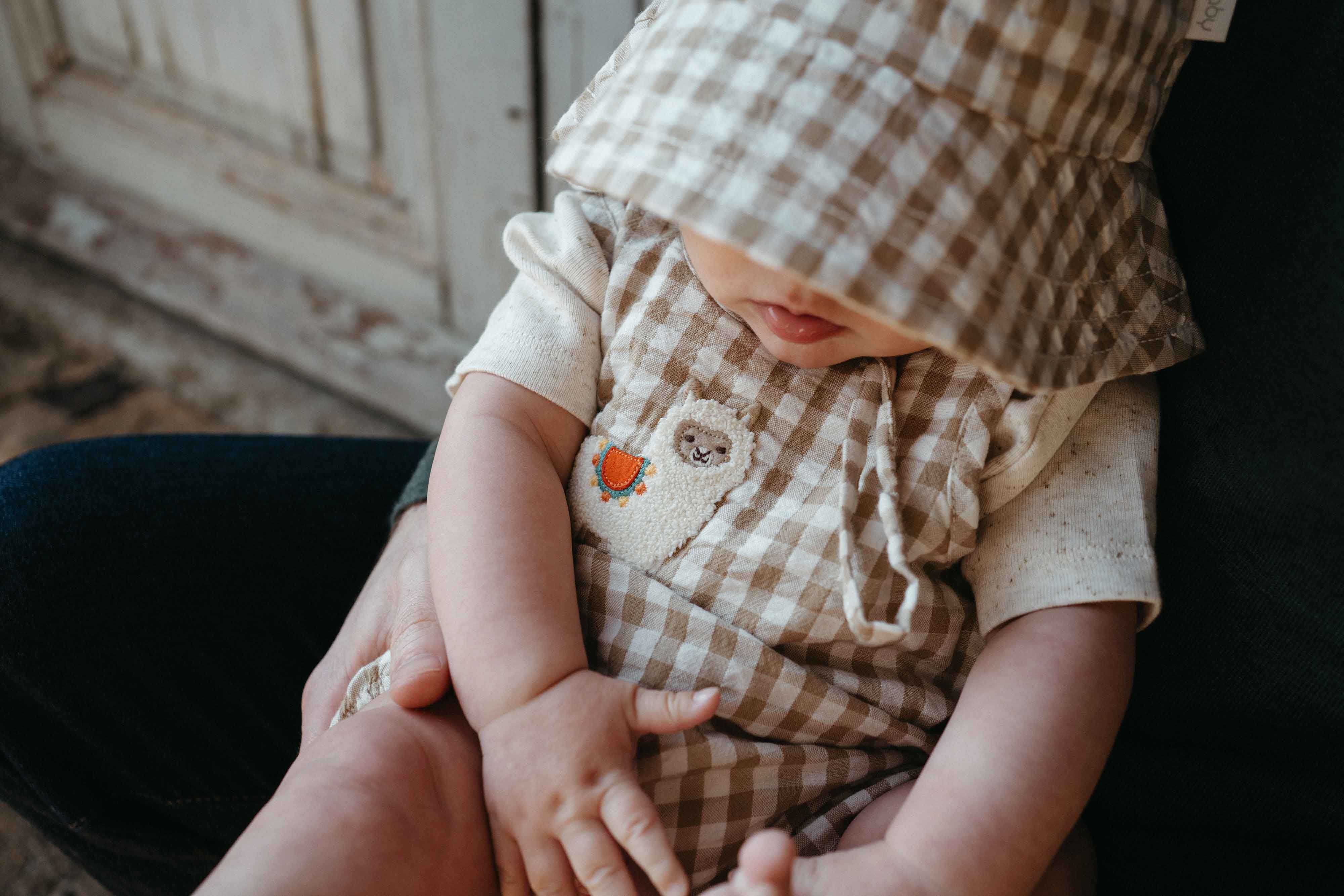 baby wearing brown and white gingham sunhat and romper