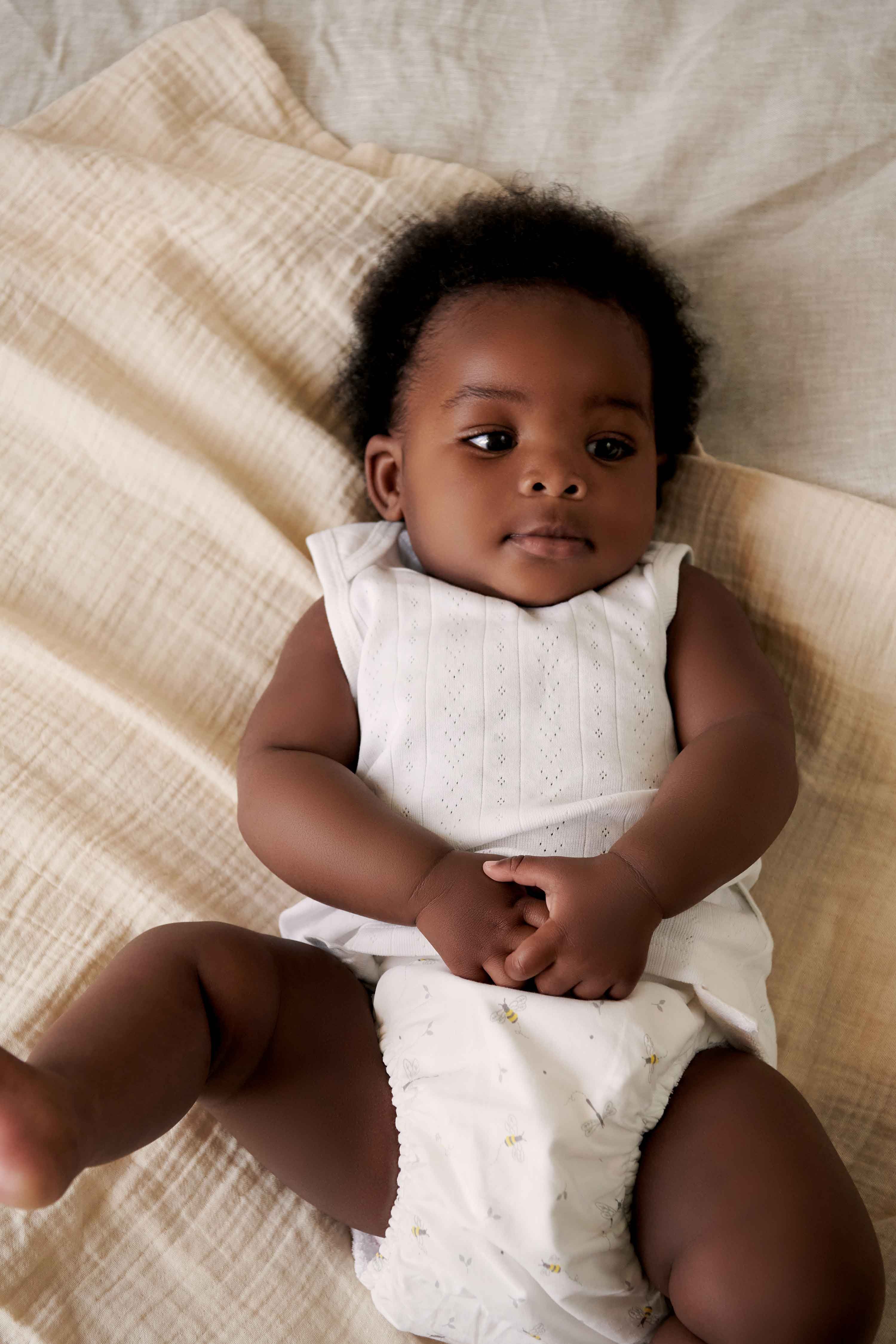 Baby laying on bed wearing white singlet and nappy