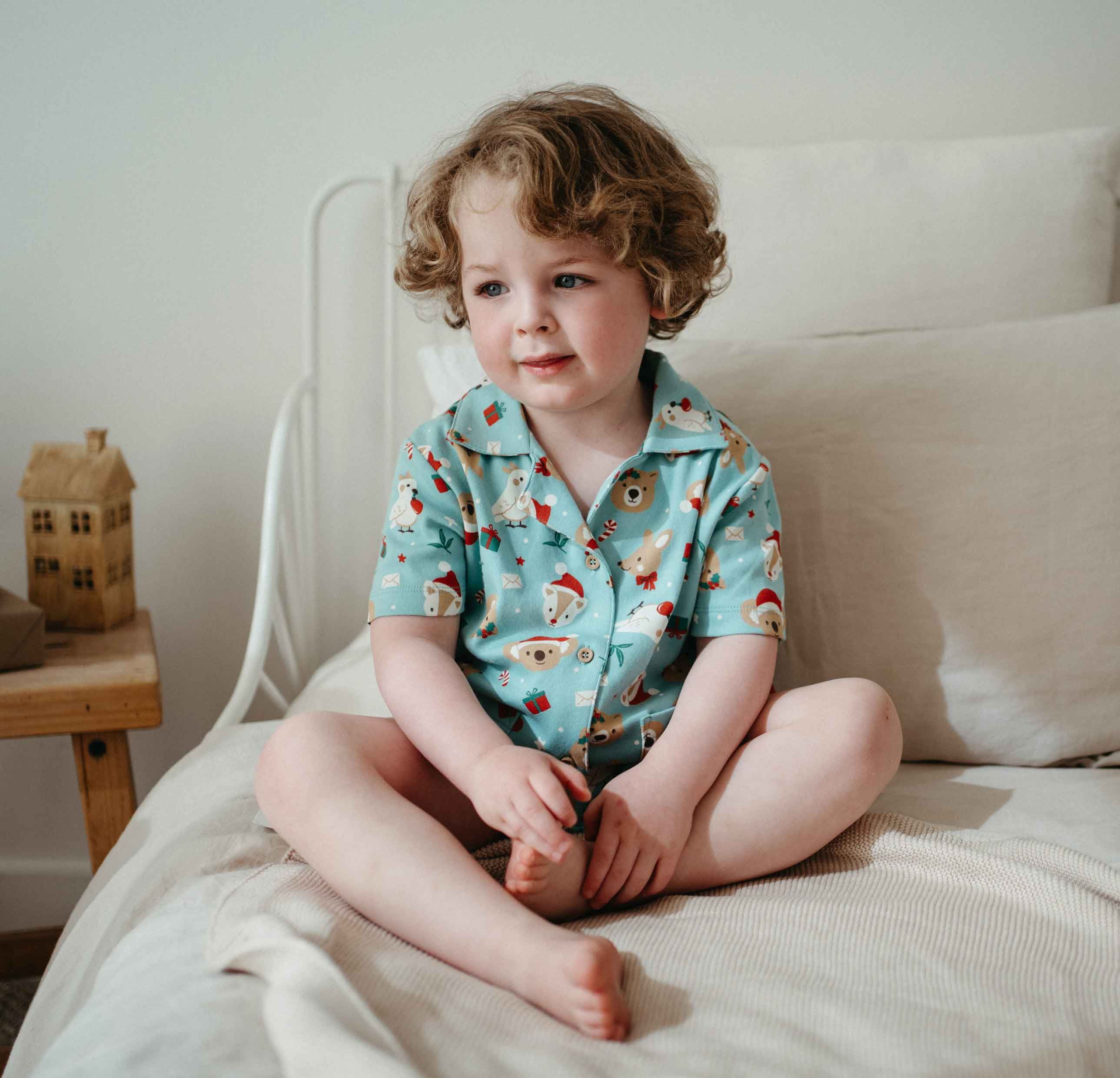 Child in Festive Friends button-up pyjama set sitting on bed