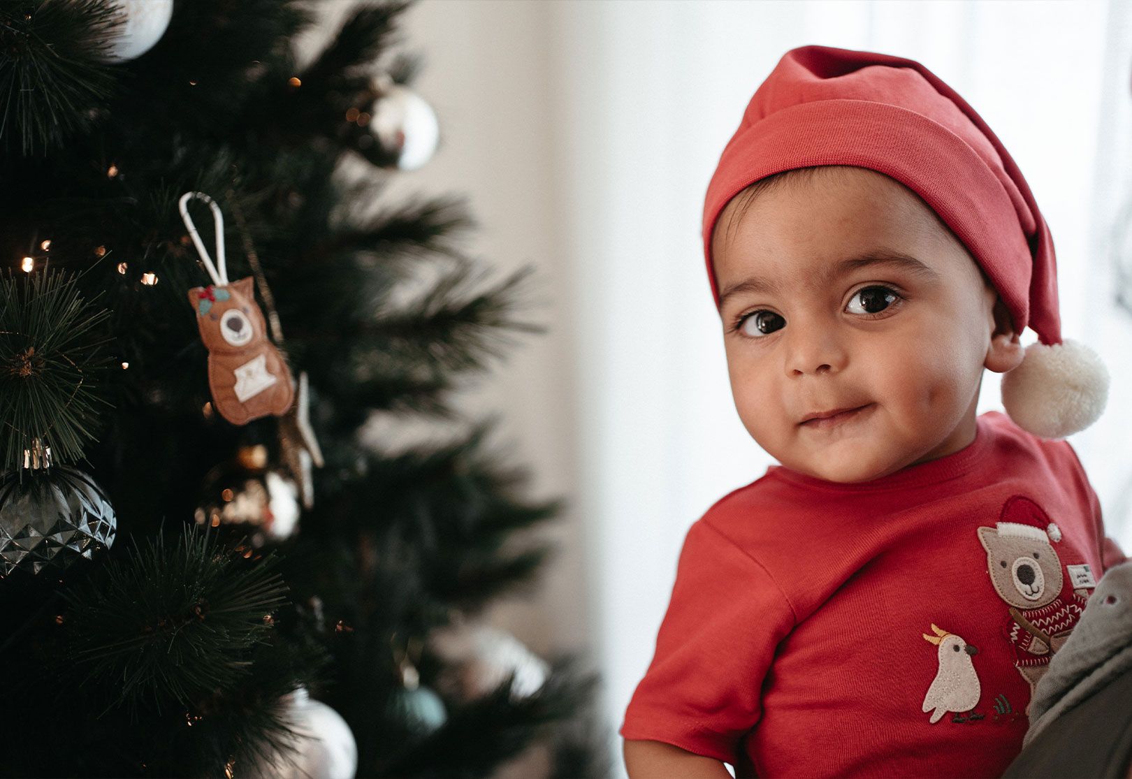Baby next to Christmas tree wearing Santa Hat
