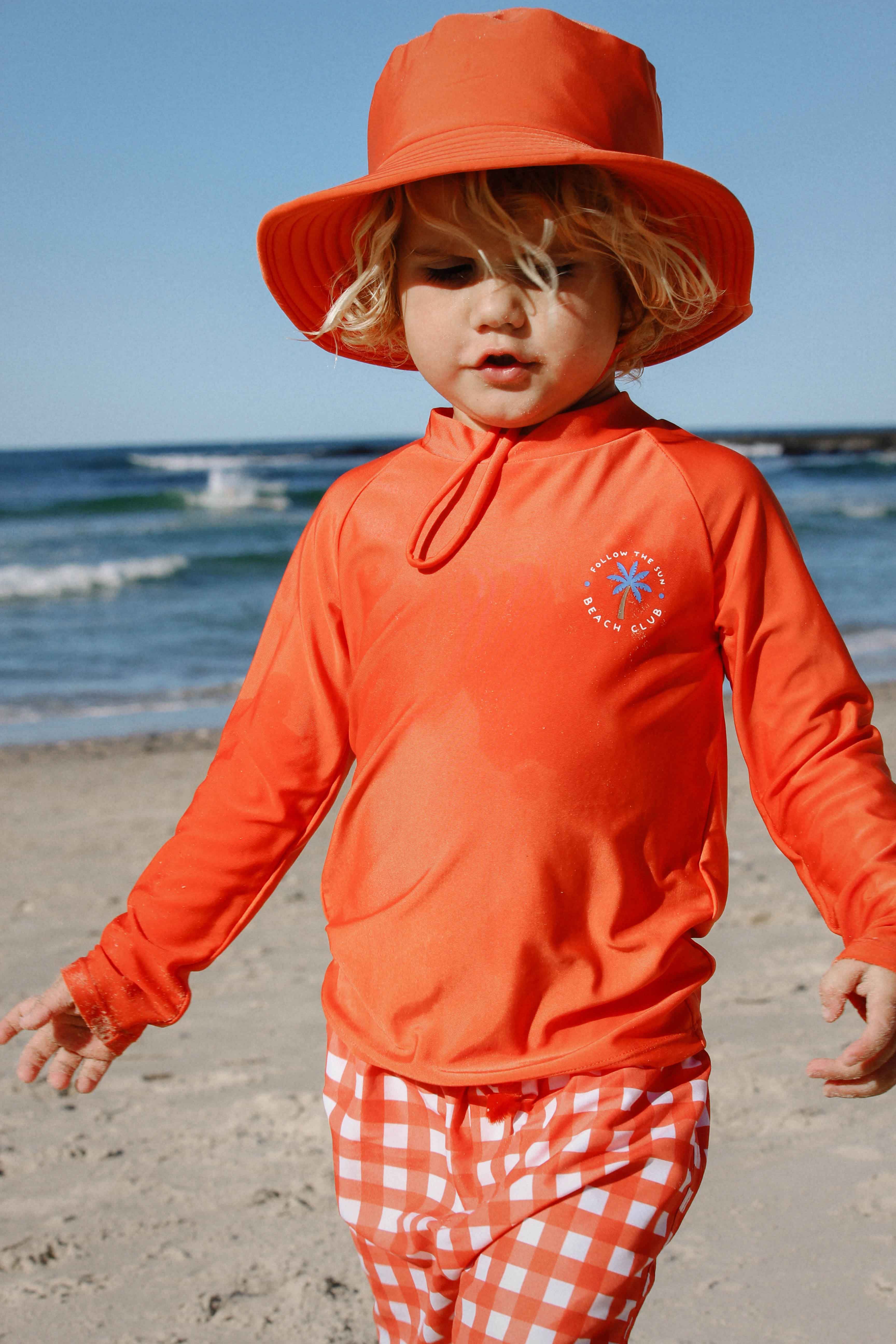 Toddler at the beach wearing a rash vest and sun hat