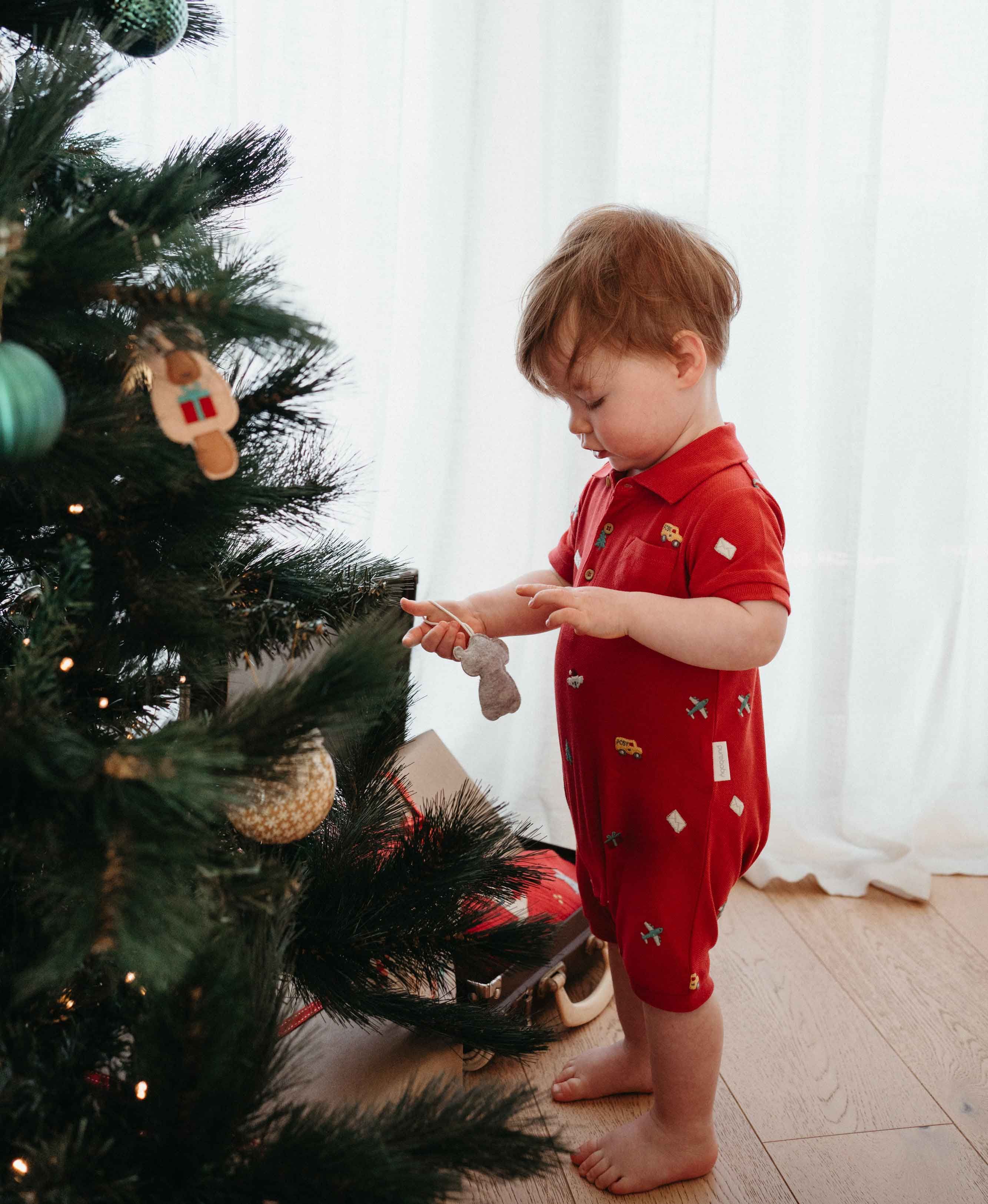 Baby in a Purebaby Christmas Polo Growsuit helping decorate the Christmas tree.