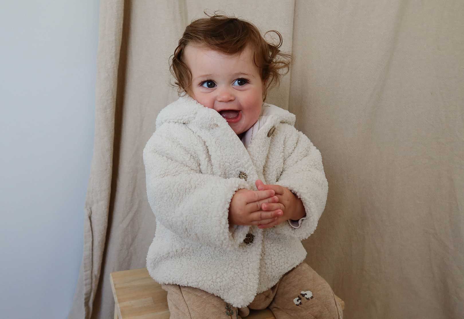 Baby wearing fluffy white jacket and brown overalls