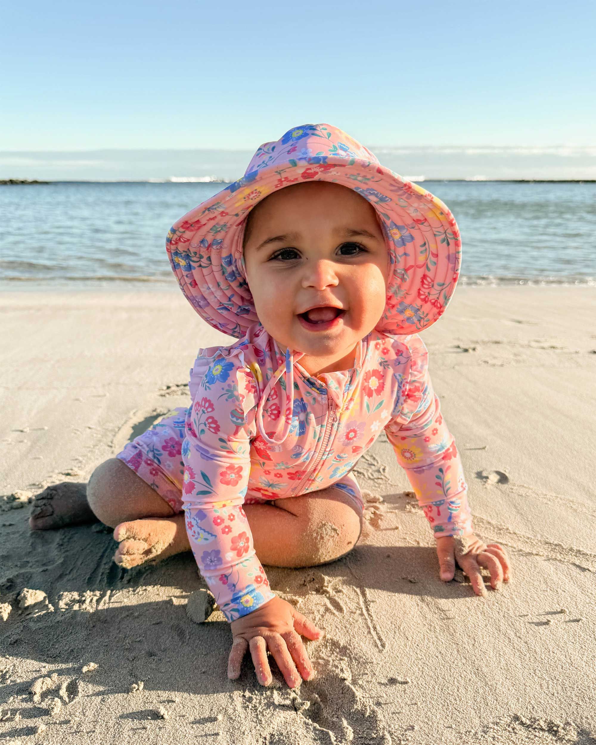 Baby in long sleeve swimsuit and sun hat playing on the sand