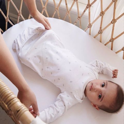 Baby laying on back in bassinet wearing Purebaby white sleeping bag