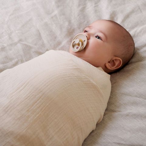 Baby swaddled in muslin wrap with a dummy in it's mouth