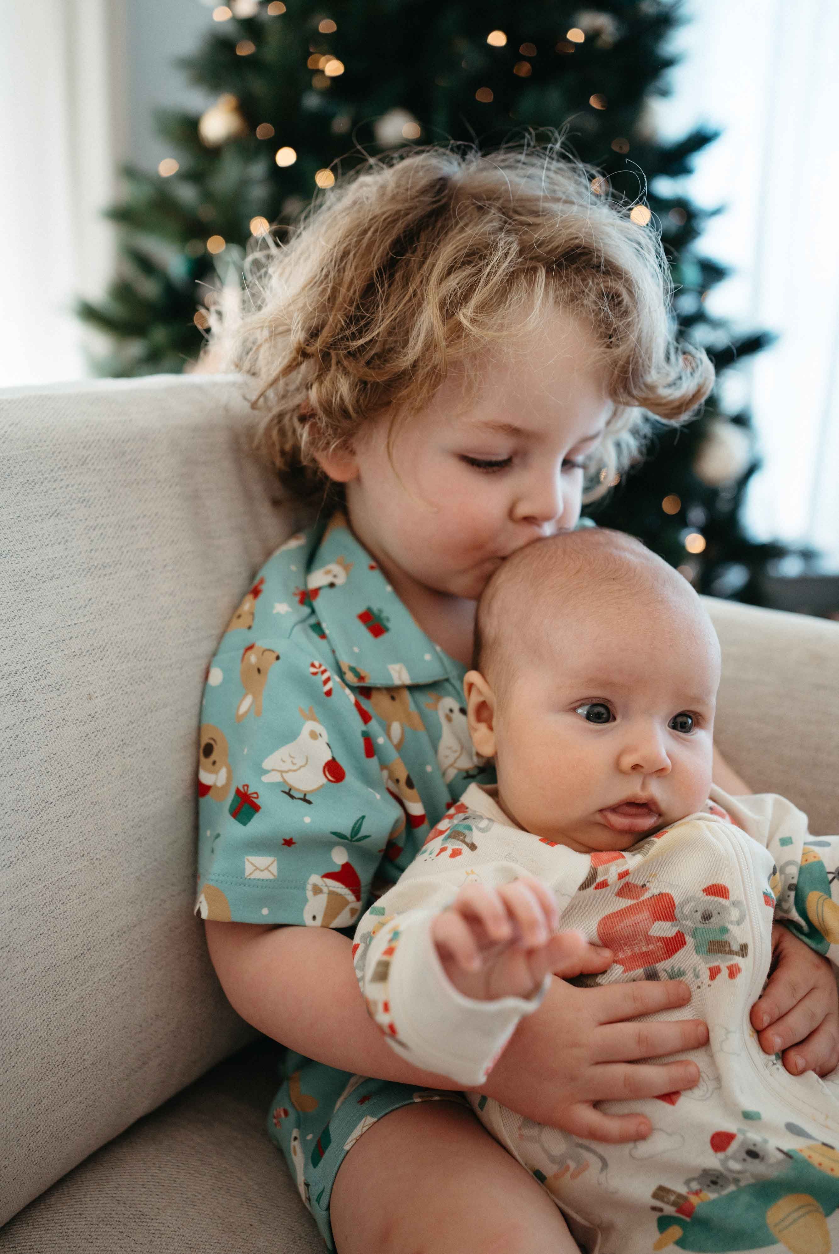 Siblings wearing matching Purebaby Christmas outfits cuddling on couch