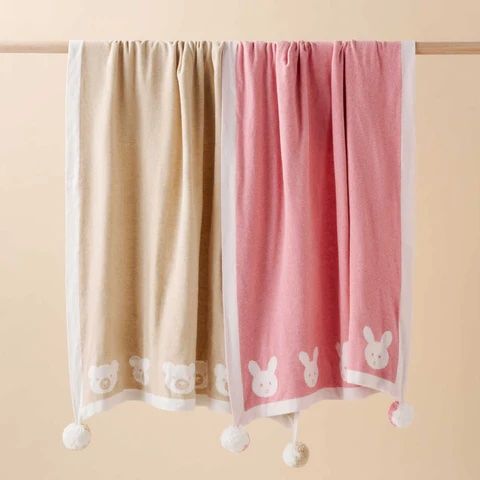 2 Purebaby blankets with pom pom details hanging from wooden rail