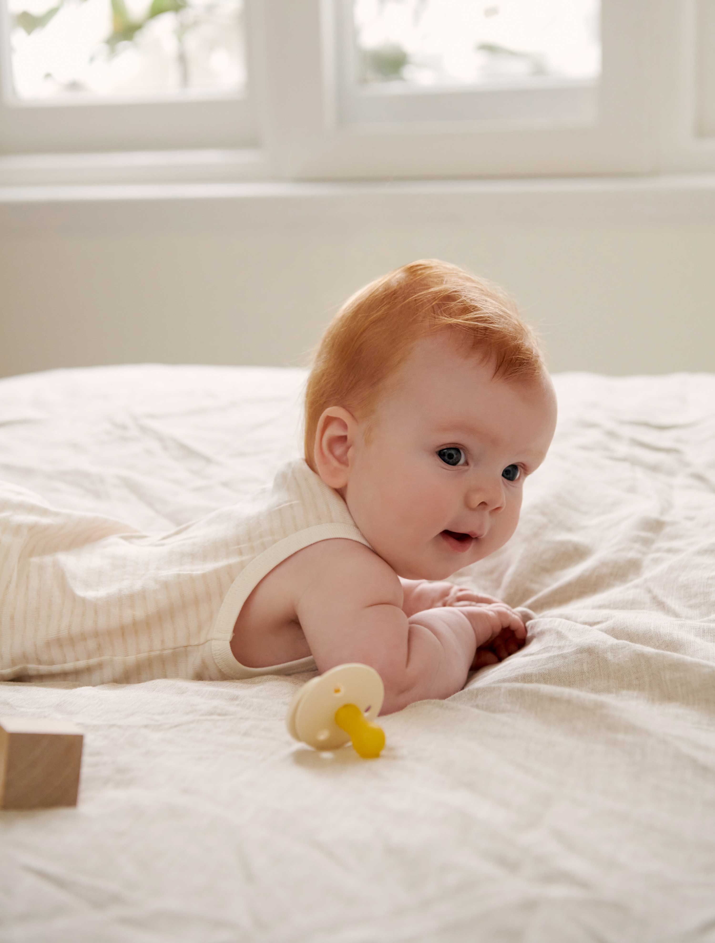 Baby laying on stomach on bed wearing bodysuit