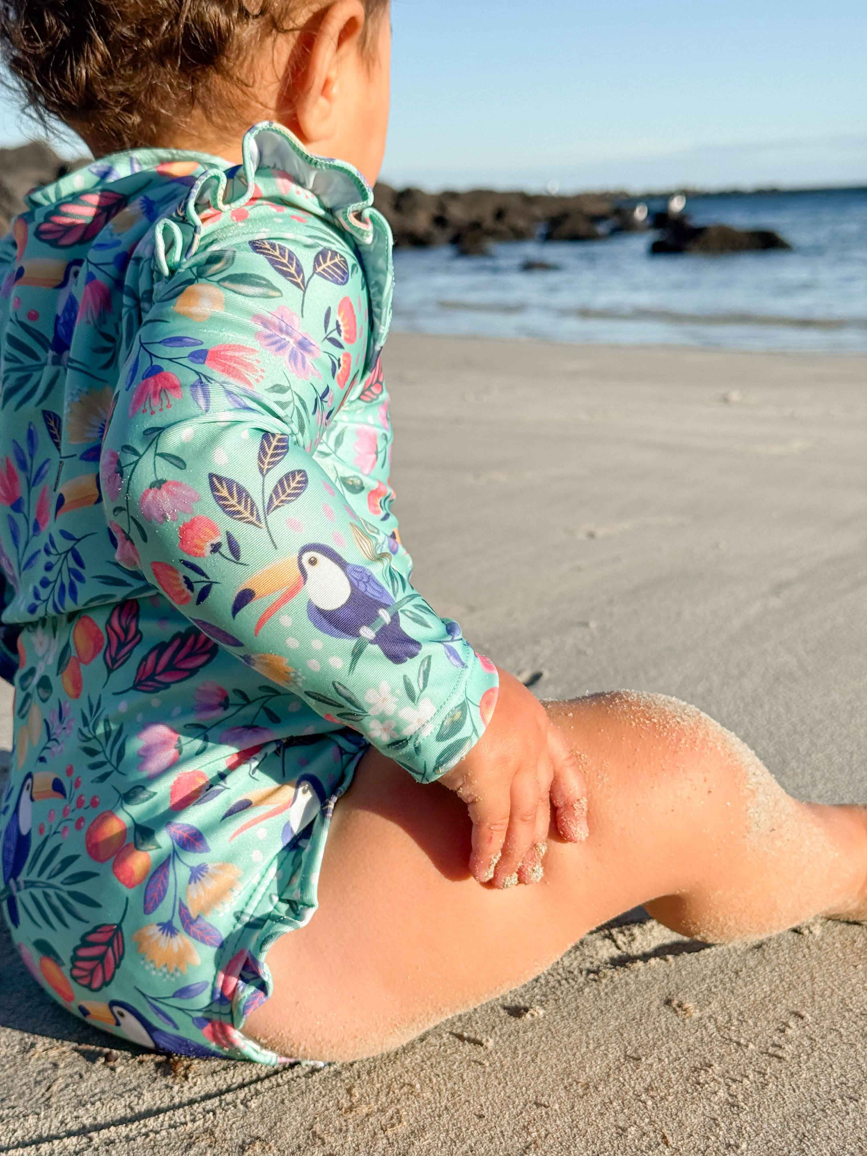 Girl playing in sand wearing Purebaby swimwear