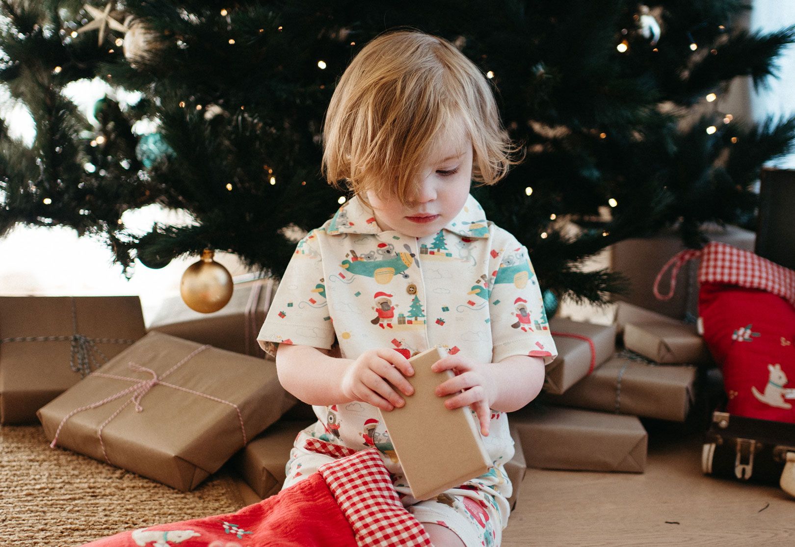 Baby next to Christmas tree wearing Christmas pyjamas opening presents