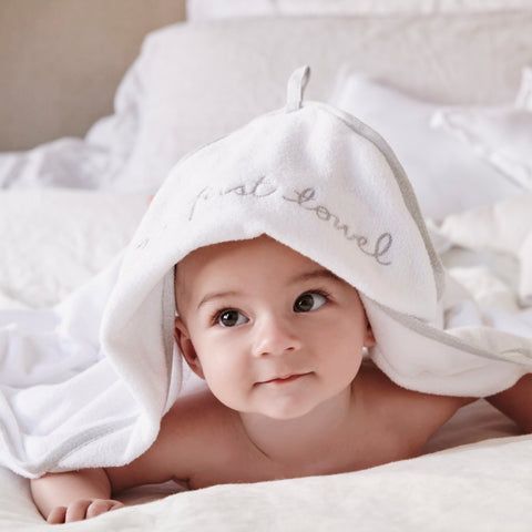 Baby laying on bed wearing Purebaby hooded towel