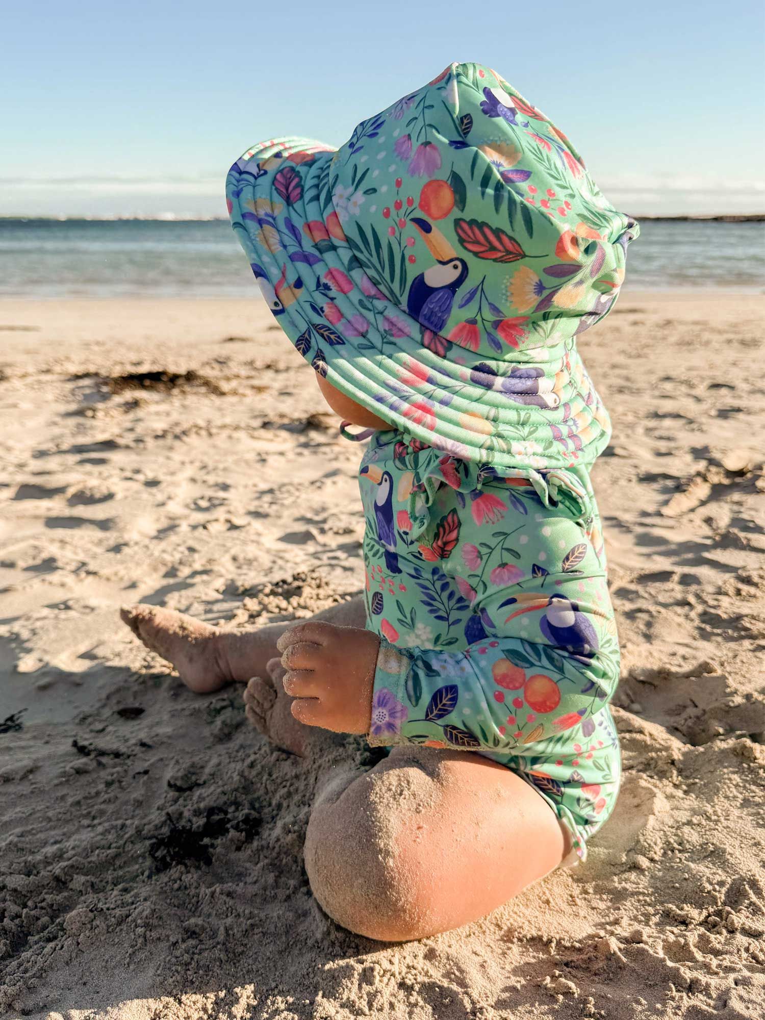 baby in Purebaby UPF 50+ swimsuit playing in the sand