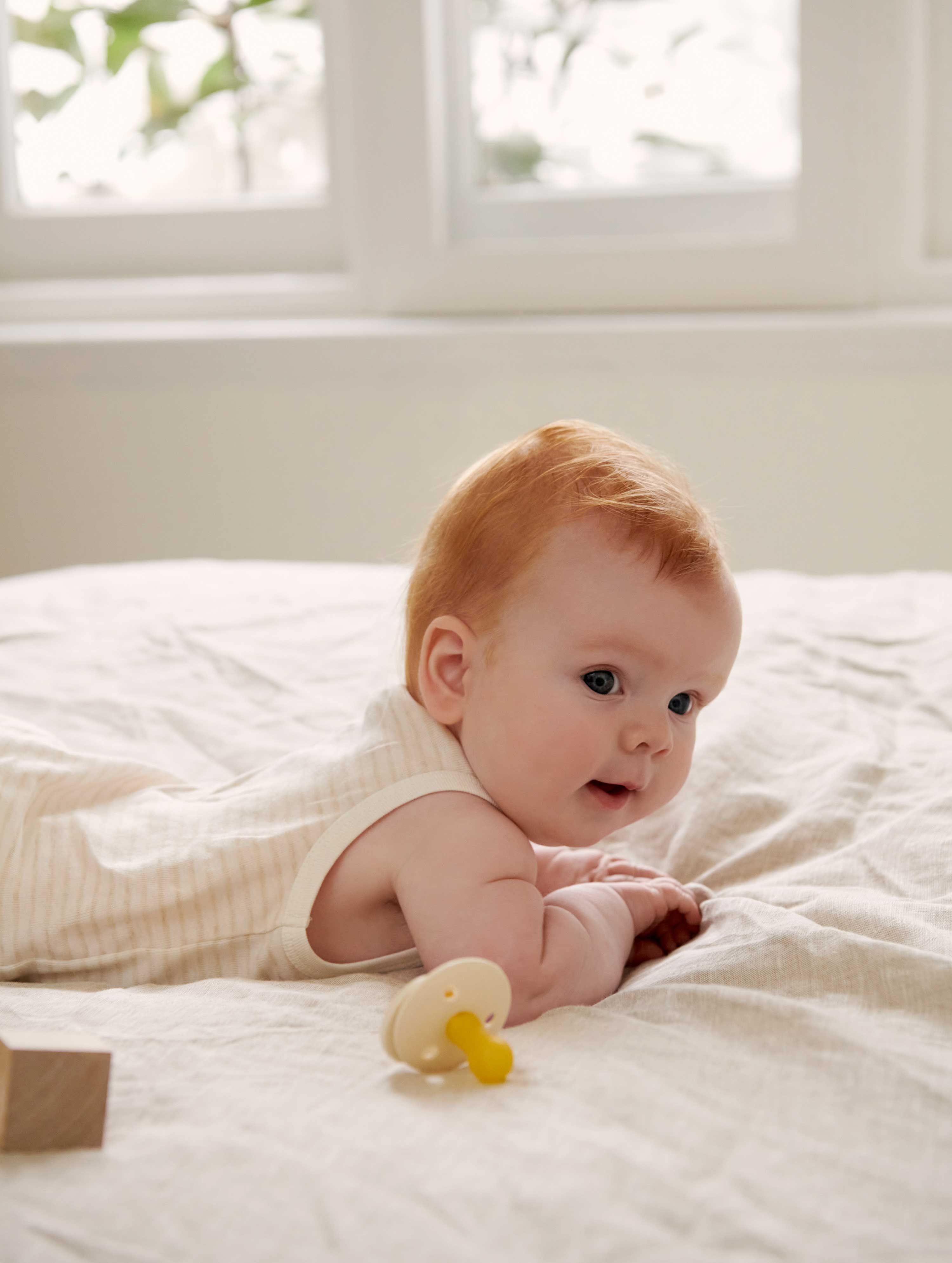 Baby laying on bed lifting chest up