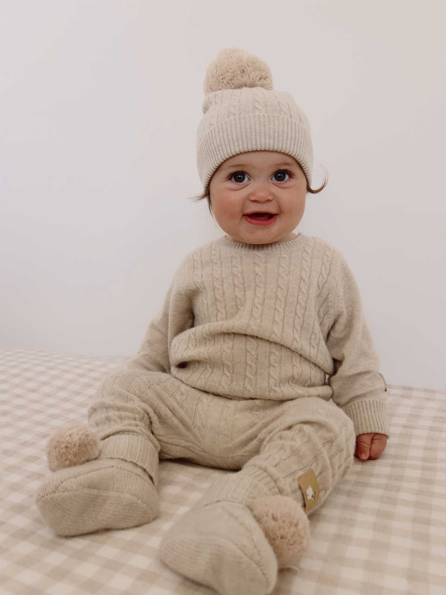 Baby wearing neutral cashmere knitted beanie, jumper, leggings and booties