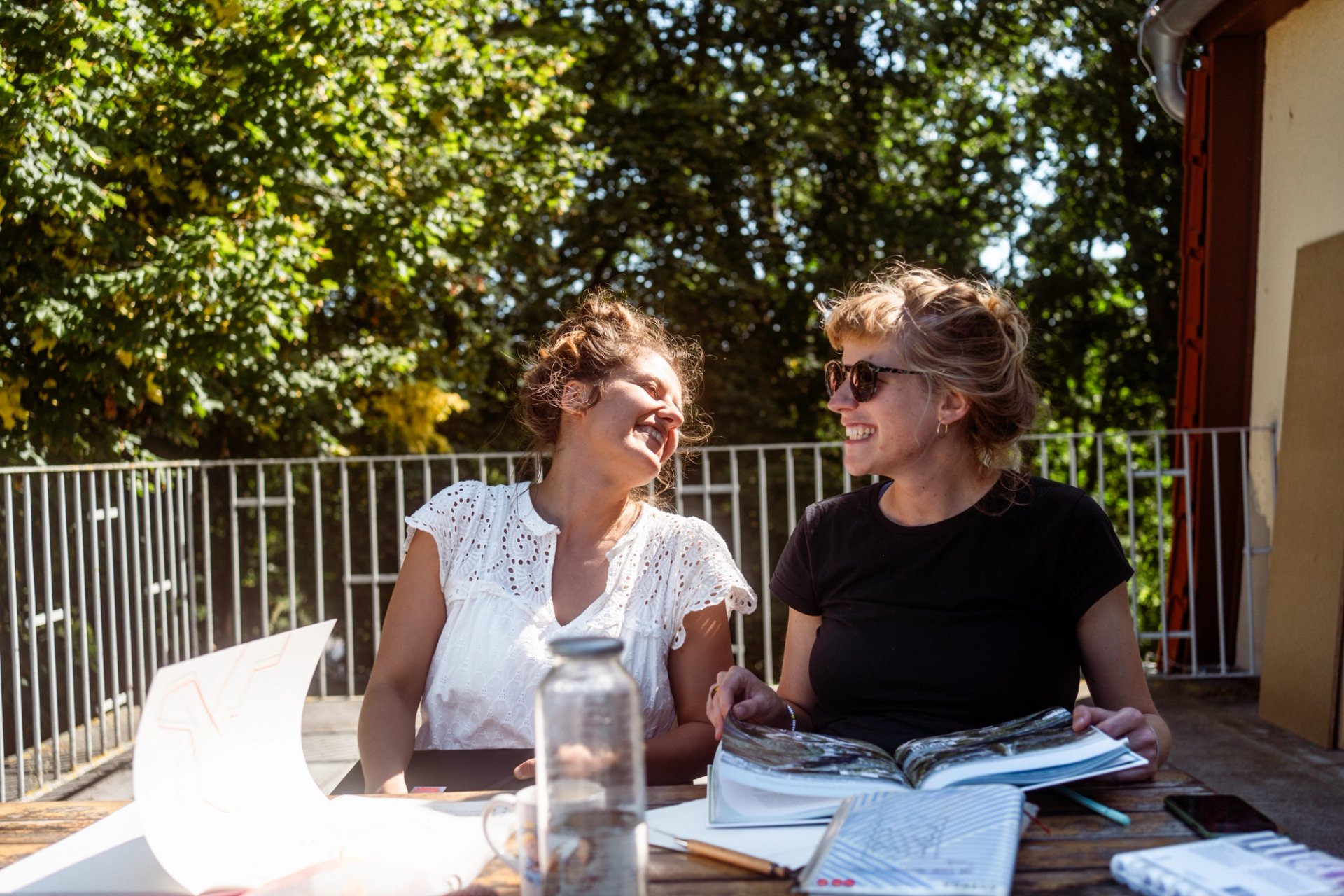 Zwei Frauen arbeiten lachend mit Unterlagen auf der Dachterrasse, Workation in Neupitz