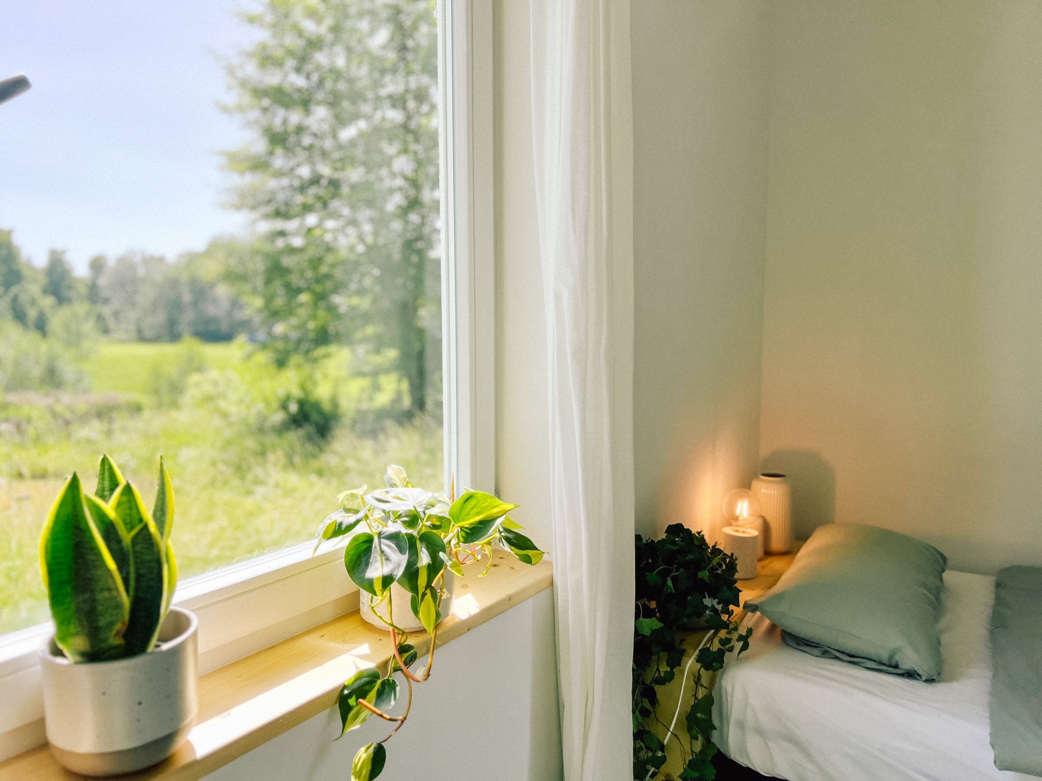 Schlafzimmer im Bungalow mit Pflanzen auf der Fensterbank und Blick ins Grüne