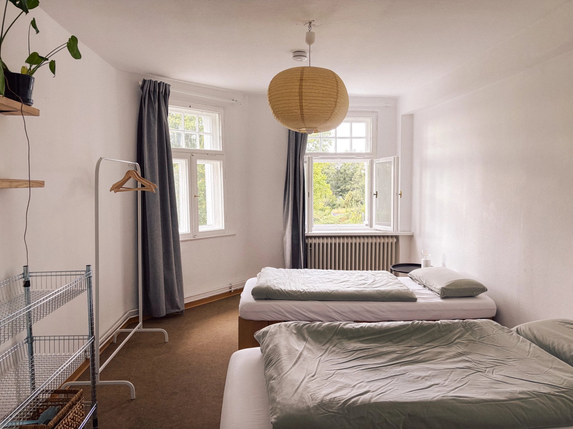 Doppelzimmer in der Villa mit zwei Betten, Kleiderstange, Papierlampe und Blick ins Grüne