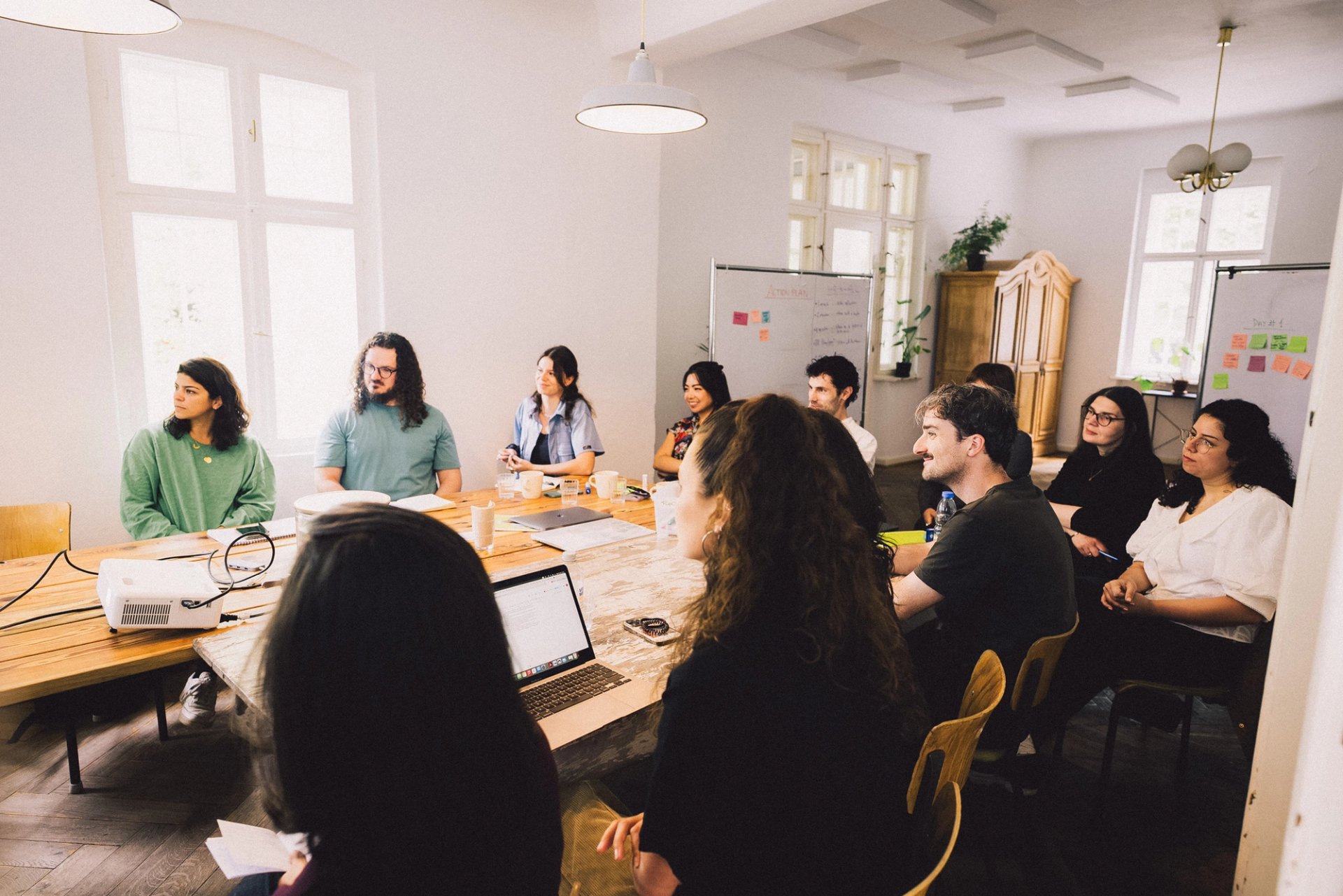 Team im Workshop am langen Tisch mit Laptops und Flipcharts, Offsite in Neupitz