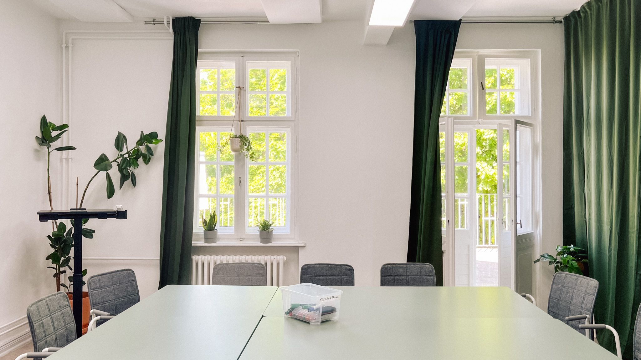 Workshopraum Seeblick mit weißem Konferenztisch, grauen Stühlen und grünen Vorhängen