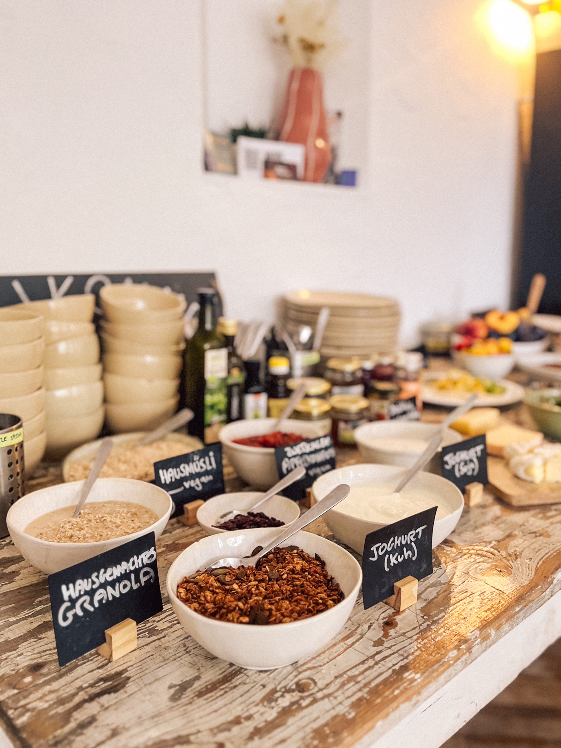 Vegetarisches Frühstücksbuffet mit Müsli und Toppings in Schalen, beschriftet mit kleinen Tafeln