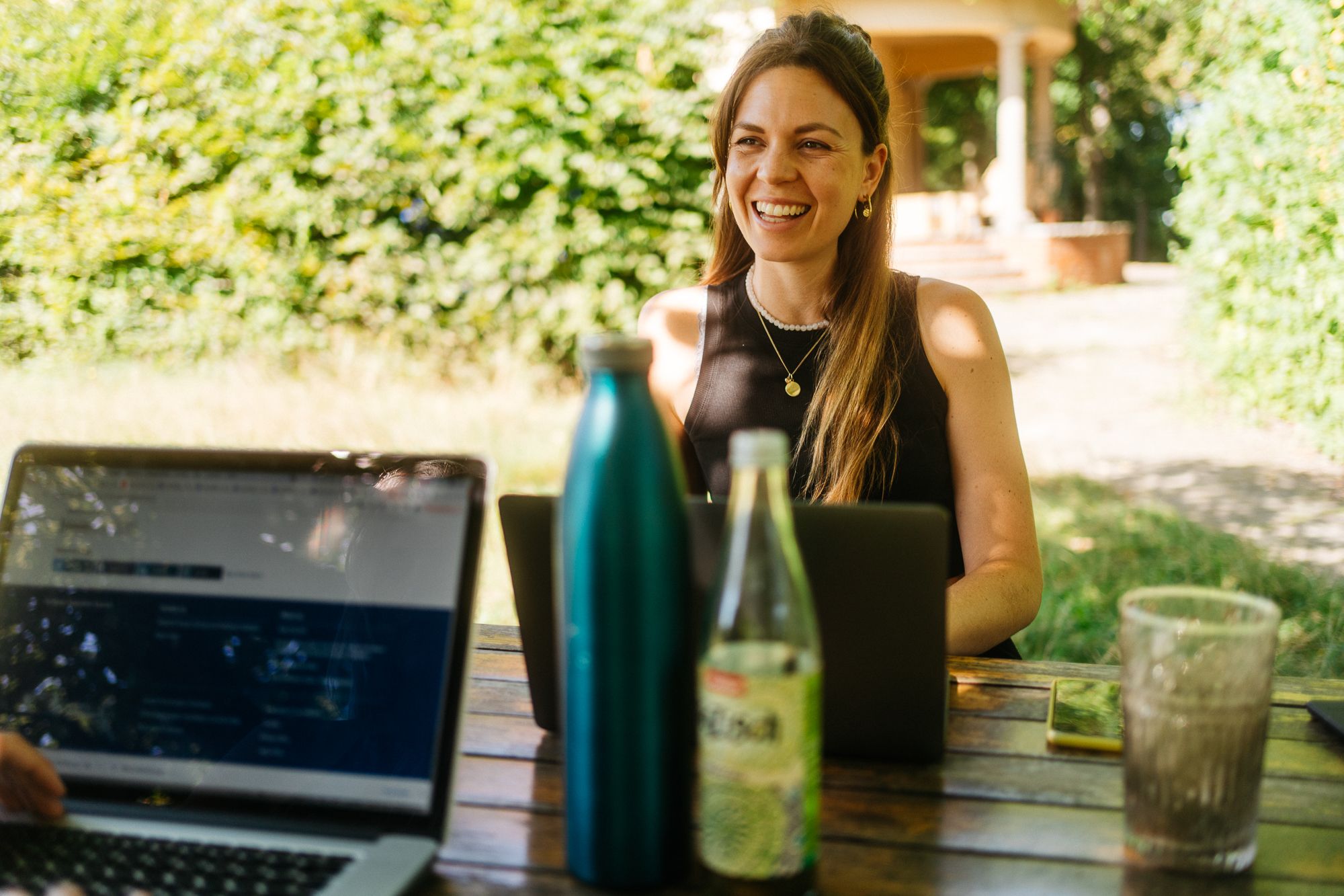 Person arbeitet lächelnd am Laptop an einem Holztisch im Garten bei einer Workation in Neupitz