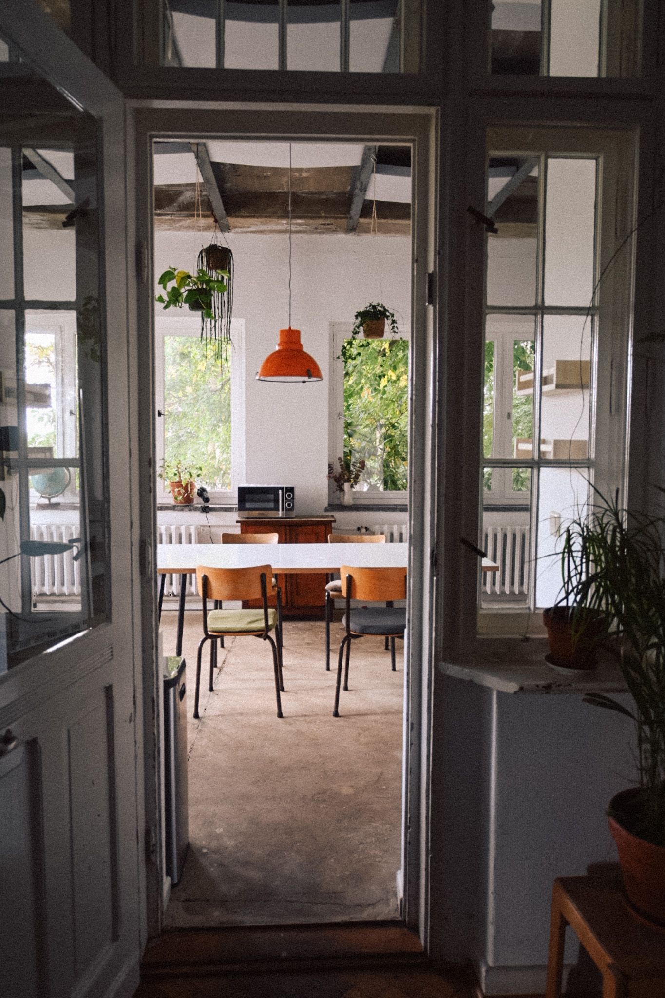 Blick in den hellen Wintergarten von Neupitz mit orangefarbener Lampe, großem Tisch und Küchenausstattung