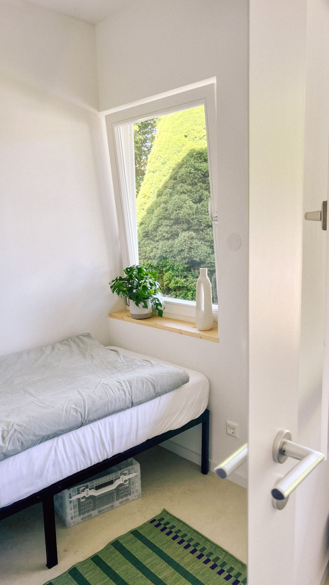 Einzelzimmer im Bungalow mit Bett, Teppich und Fenster mit Pflanze, Unterkunft für Workation und Team-Retreat