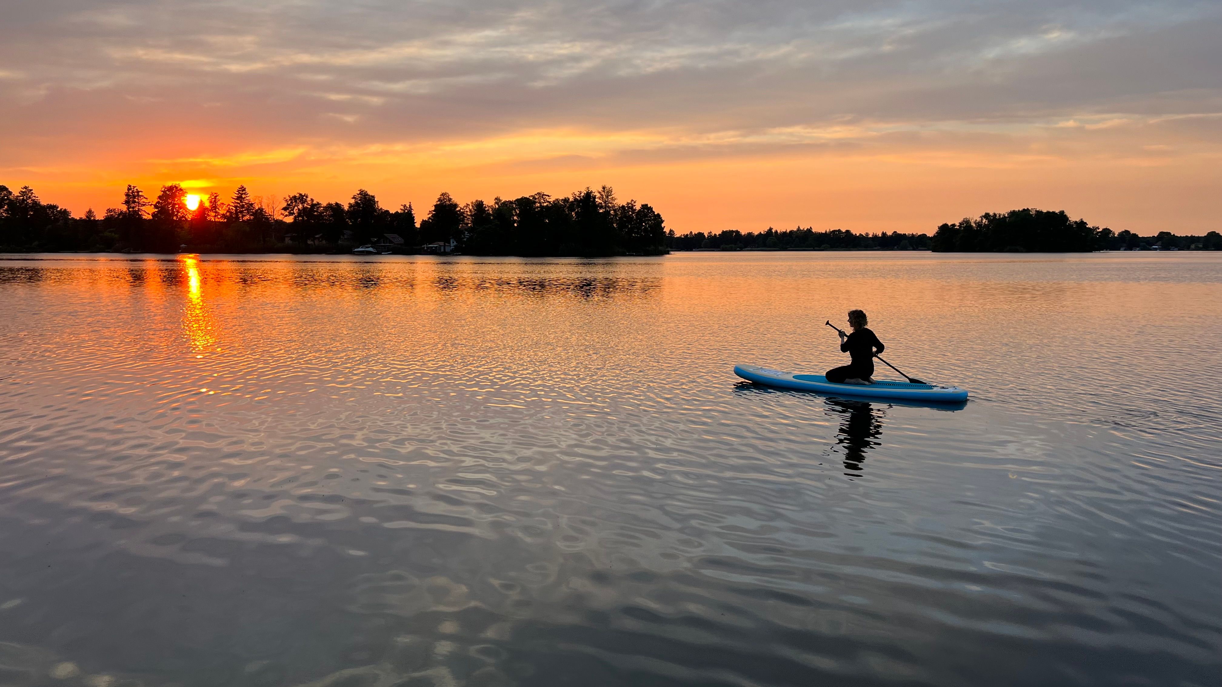 Person auf dem Stand-up-Paddle-Board bei Sonnenuntergang auf dem Teupitzer See