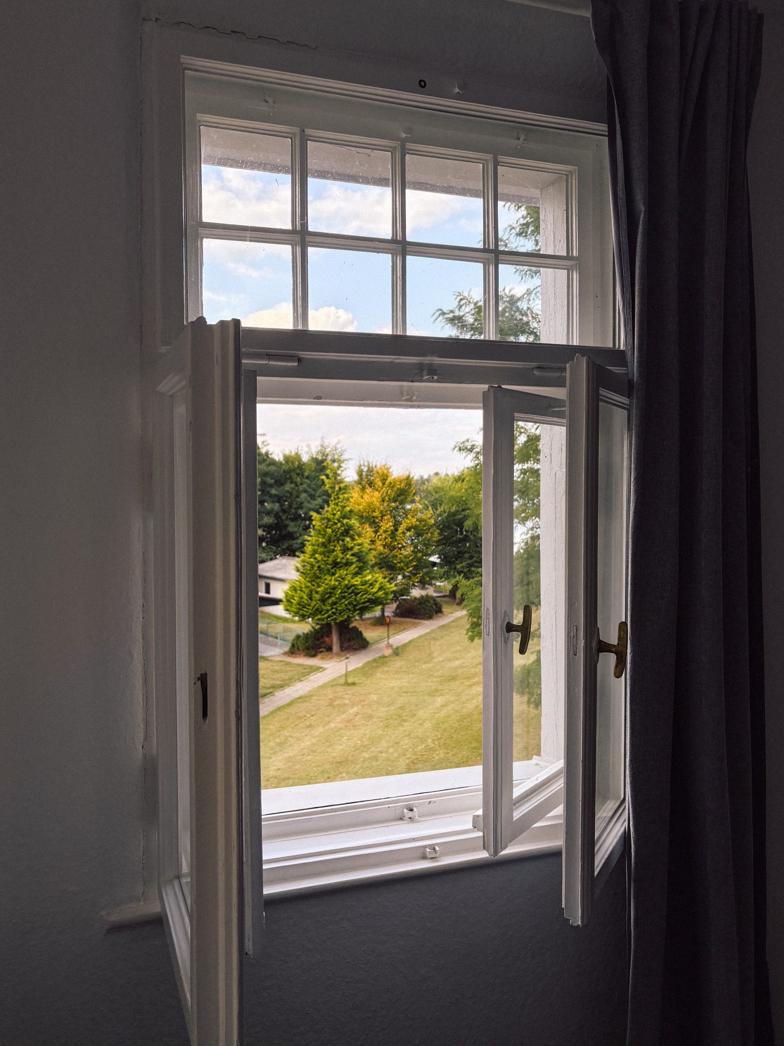 Geöffnetes Fenster im Zimmer der Villa mit Blick über die Wiese auf die Bungalows